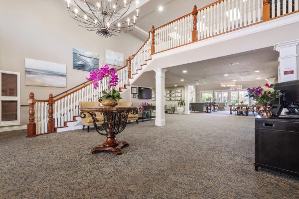 A large staircase at the entrance of Aptos. In the middle of the room is a table with pink flowers on it, and above that is a large chandelier.