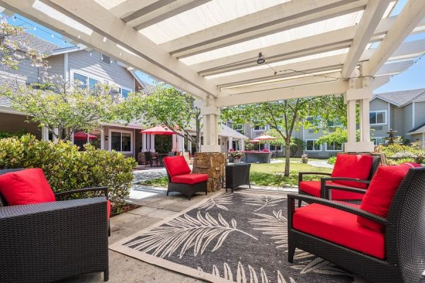 A covered outdoor seating area with four red chairs and a blue, leaf-patterned rug.