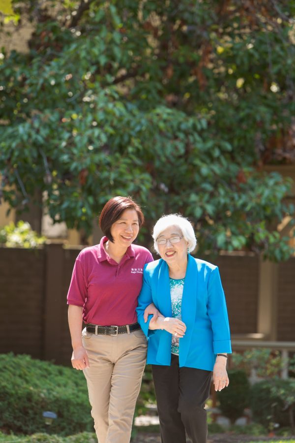 An older lady walking outside with a staff member.