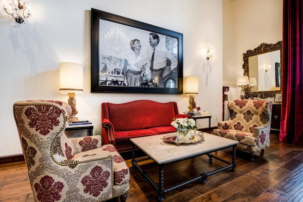 A small seating area with a red couch, two armchairs, a coffee table, and a large movie poster