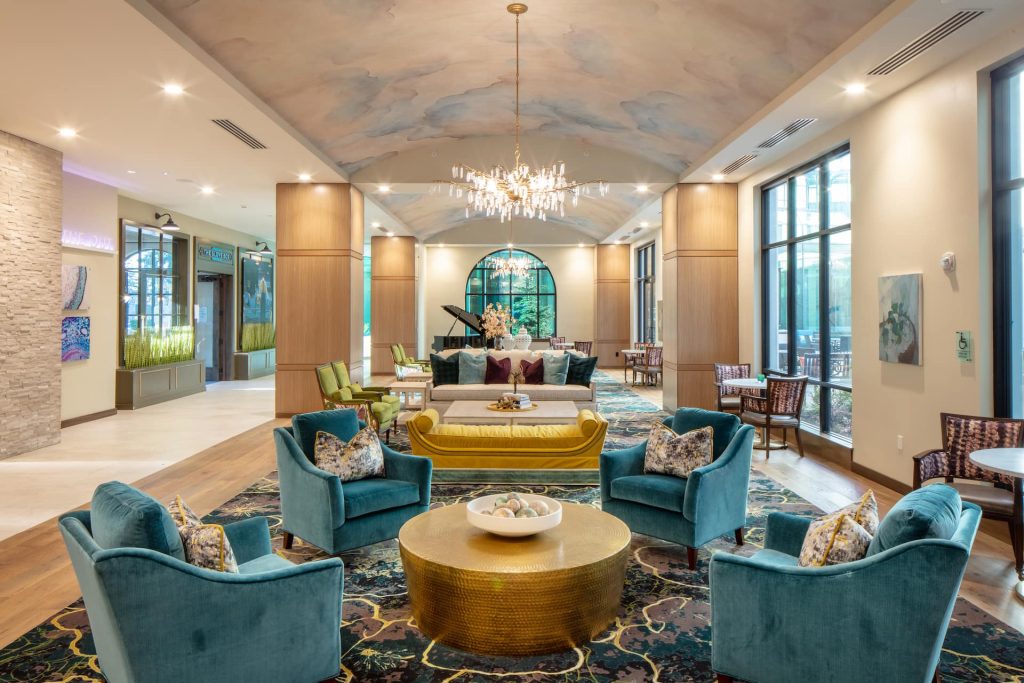 A large seating area with green velvet chairs, a gold coffee table, and a chandelier.