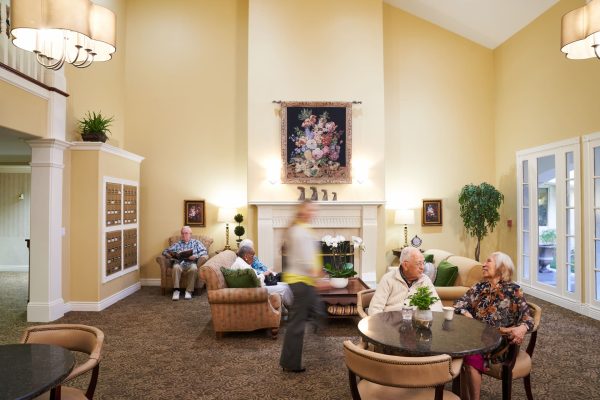Residents sitting and talking in a living room with couches, tables, chairs, and a fireplace