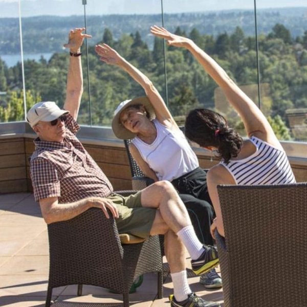 Three residents, two women and one man, sitting and stretching, with Lake Union in the background