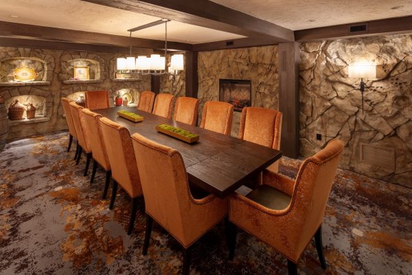 A long brown dining table with orange velvet chair in a cozy cavernous room.