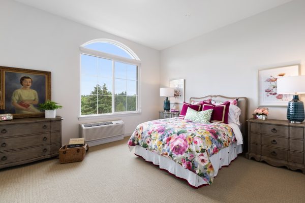 A large bedroom with a big window, a bed with pink floral sheets, and two brown dressers.