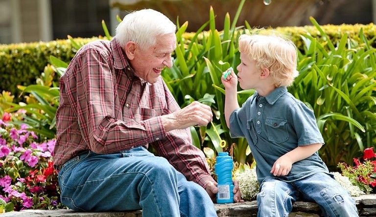 Elderly man laughs as young boy blows soap bubbles
