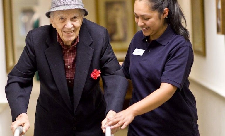 An Aegis Living staff assisting a resident walk with a walker