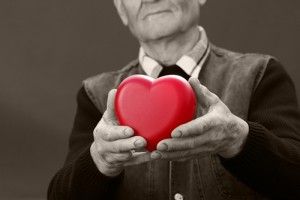 Black and white image of a senior man holding a fake pink heart.