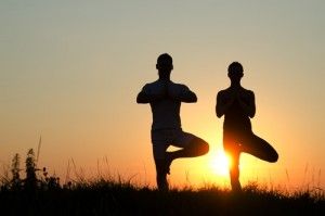 Two people doing tree yoga pose with the sunset in the background