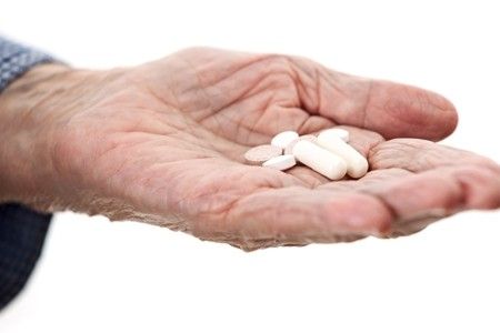 an elderly hand holding white pills.
