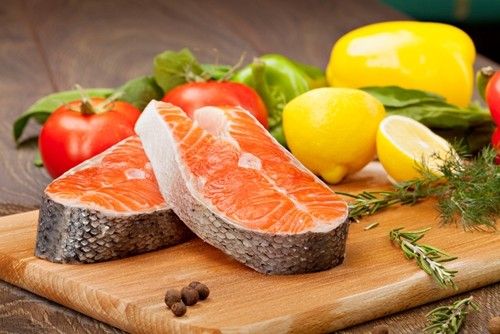 delicious cuts of fish on a cutting board with assorted vegetables and sliced lemon