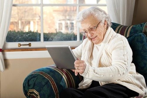 a senior woman with a white sweater reading by the window.