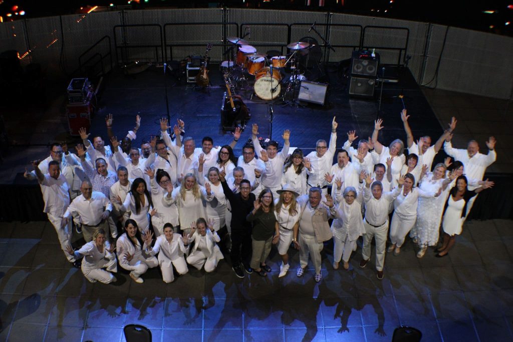 A group of Aegis Living employees wearing white, throwing their hands in the air, and smiling for the camera