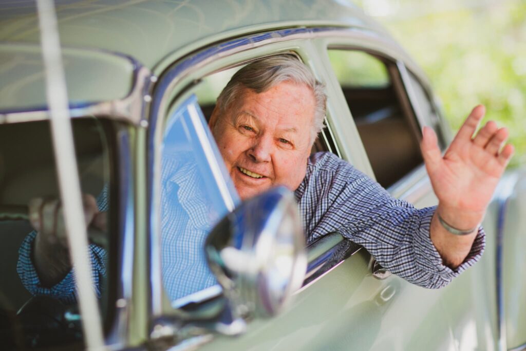 A resident sitting in a classic car and waving out the window