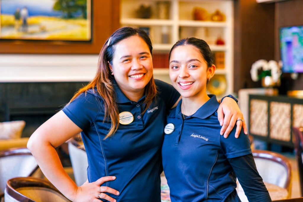 Two Aegis Living employees, smiling with their arms around each other